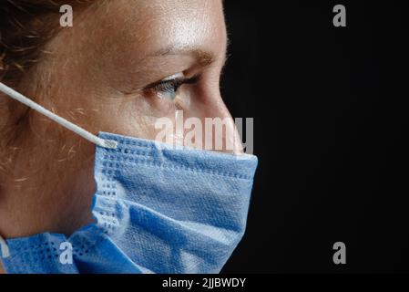 Porträt eines müden oder traurig depressiven Arztes in Nahaufnahme auf schwarzem Hintergrund. Ein dramatisches Porträt eines Arztes. Arzt bei der Arbeit müde. Krankenschwester in Stockfoto