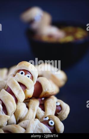 Tolles Essen für Kinder. Mama Hot Dogs (oder Schweine in einer Decke) auf einem blauen rustikalen Tisch mit einer Schüssel Ketchup und Senfdip, mit Spinnennetz-Design. Wählen Sie Stockfoto