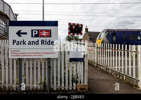 Park-and-Ride-Schild an einem Bahnhof mit Zug- und Bahnübergangsbeleuchtung im Hintergrund in Cardross, Argyll und Bute, Schottland, Großbritannien Stockfoto