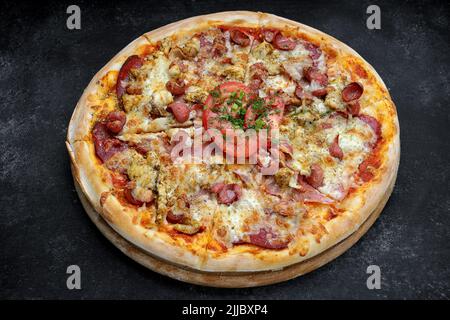 Pizza mit Wurstfleisch und Huhn, Käse und Tomaten auf grauem Beton-Hintergrund, mit selektivem Fokus. Horizontal Stockfoto