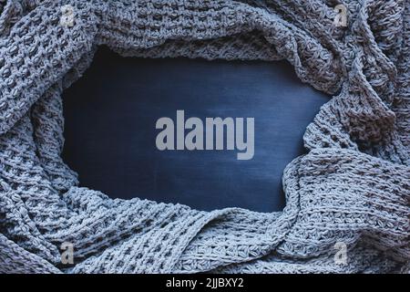 Grau gewebte Decke zerknittert und gerahmt auf einem dunklen schwarzen Holzhintergrund. Aufnahme von oben mit freiem Platz für Hintergrundtext. Stockfoto