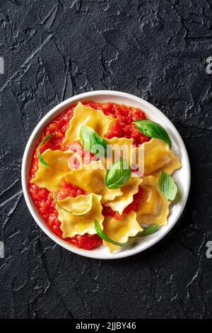 Ravioli mit Tomatensauce und frischem Basilikum, italienische Knödel, Top Shot auf einem schwarzen Tisch Stockfoto