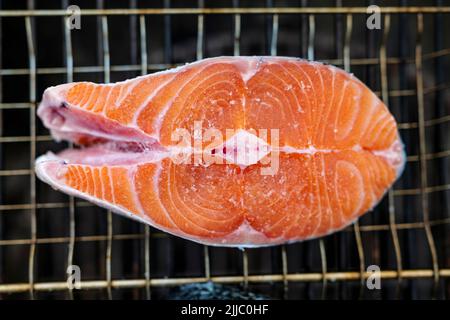 Nahaufnahme von frischem Lachssteak, das zum Grillen mit Salzkörnern darauf zubereitet wird, liegt auf dem Grillgitter Stockfoto