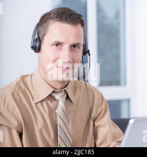 Ein freundlicher Mann mit einem Headset arbeitet im Home Office an einem Computer Stockfoto