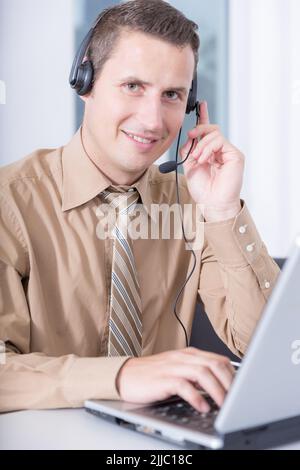 Ein freundlicher Mann mit einem Headset arbeitet im Home Office an einem Computer Stockfoto