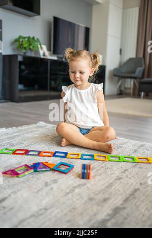 Kleines Mädchen spielen bunte Magnet Kunststoff-Blöcke-Kit zu Hause. Das Kind spielt pädagogische Spiele. Frühkindliche Entwicklung. Stockfoto