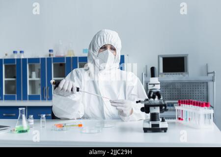 Wissenschaftler im Gefahrstoffanzug, der in der Nähe von Reagenzgläsern im Labor mit Pipetten und Glas arbeitet Stockfoto