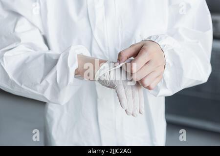 Beschnittene Ansicht eines Wissenschaftlers in einem Hazmat-Anzug, der im Labor den Latexhandschuh auszieht Stockfoto