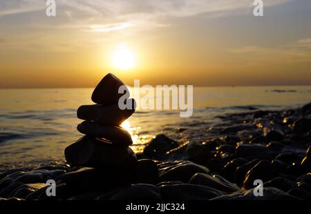 Hochauflösende Bilder von schwarzen Stapelsteinen vor verschwommenem Hintergrund des Sommermeeres Stockfoto