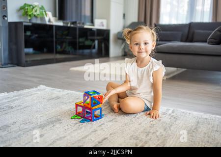 Kleines Mädchen spielen bunte Magnet Kunststoff-Blöcke-Kit zu Hause. Das Kind spielt pädagogische Spiele. Frühkindliche Entwicklung. Stockfoto