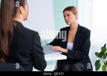 Geschäftstreffen. Junge blonde Frau, die während eines Unternehmensmeeting vor dem Berater sitzt, einen Vertrag hält. Der Chef diskutiert Ideen mit dem Unternehmen Stockfoto