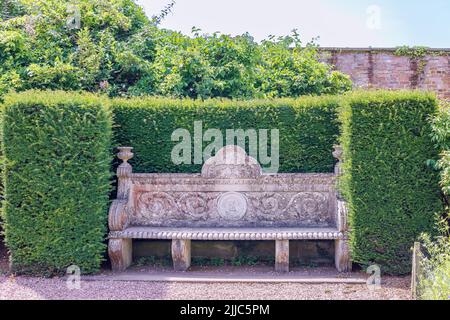 In einer abgeschiedenen Ecke des Tatton Park, Großbritannien, befindet sich eine aus Stein gemeißelte Vintage-Gartenbank mit Akanthus-Blättern und Schriftrollen. Stockfoto