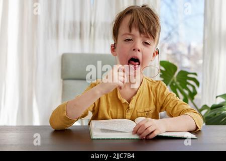 Gelangweilt kleinen Schüler Gähnen während des Lesens zu Hause Stockfoto