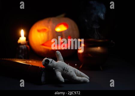 Halloween Kürbis mit brennendem Mund, Buch und einer Voodoo Puppe - Volt auf dunklem Hintergrund. Halloween-Konzept. Stockfoto