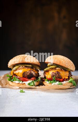 Superleckere, handgefertigte, saftige Cheeseburger mit gegrilltem Paprika, Rucola, Sauce und Gurken auf Holzboden. Platz für Text oder Design e kopieren Stockfoto