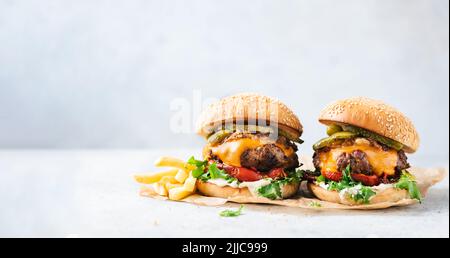 Zwei handwerkliche Cheeseburger und Pommes auf Pergamentpapier auf grauem Betongrund. Speicherplatz kopieren. Webbanner Burger Stockfoto