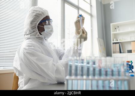 Nahaufnahme einer Wissenschaftlerin, die vollständige Schutzkleidung trägt, während sie im medizinischen Labor mit gefährlichen Materialien forscht Stockfoto