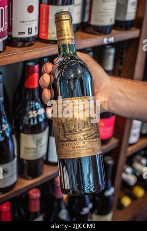 Die Hand des jungen Mannes hält eine teure Vintage-Rotwein-Flasche Stockfoto
