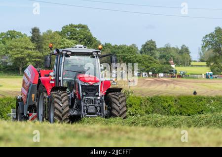 Großes Ballengras auf einer Wiese mit einem Massey Ferguson-Traktor und einer Ballenpresse mit Verpackung 3130DF. Dumfries, Schottland. Stockfoto