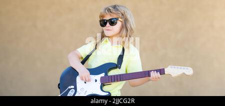 Kindermusiker spielt Gitarre wie ein Rockstar im Freien. Kid Boy Rockmusiker mit Gitarre. Kinder Musikinstrumente, Banner. Stockfoto