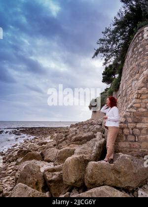 La Rochelle, Frankreich Juni 2022. Eine Touristenfrau blickt auf die Wolken und das Meer an einem felsigen Kai in La Rochelle Stockfoto