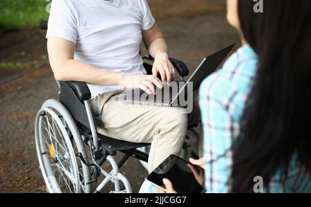 Mann im Rollstuhl und Frau arbeiten im Park aus der Ferne Stockfoto
