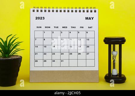 Tischkalender Mai 2023 mit Tischpflanze und Minutenglas auf gelbem Hintergrund. Kalenderkonzept Stockfoto