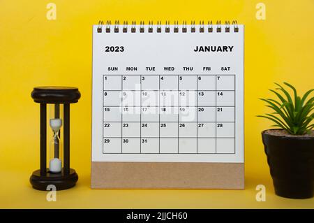 Januar 2023 Tischkalender mit Tischpflanze und Minutenglas auf gelbem Hintergrund. Kalenderkonzept Stockfoto