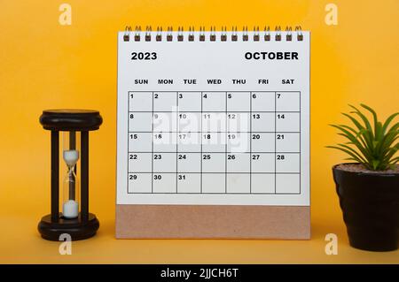 Oktober 2023 Tischkalender mit Minutenglas und Pflanze auf gelbem Hintergrund. Kalenderkonzept Stockfoto