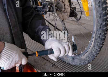 Nahaufnahme eines Mannes, der das Rad auf der Straße pumpt. Fahrradreparatur, Fahrradfahrer Pumpen Reifen. Der Mann pumpt das Rad mit einer Pumpe auf. Pumpende Luft Stockfoto