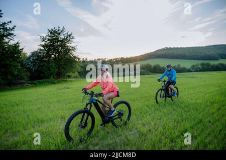 Aktives Seniorenpaar, das auf dem Trail im Sommerpark Elektrofahrräder fährt, gesundes Lifestyle-Konzept. Stockfoto