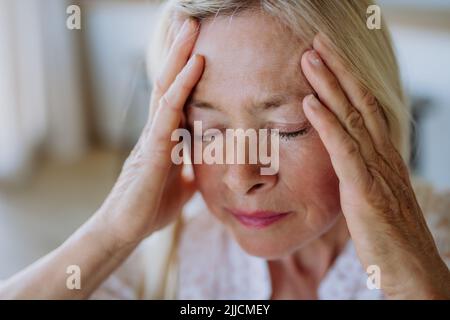Porträt einer attraktiven älteren Frau, die zu Hause mit Kopfschmerzen auf einem Sofa sitzt Stockfoto