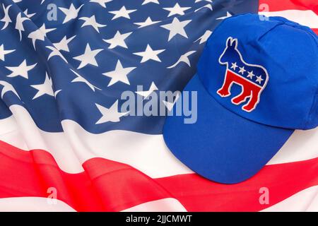 Blaue DNC-Kappe mit dem Esel-Emblem und US Stars and Stripes Flagge. Für die Präsidentschaftswahlen 2024 in den USA und die Vernichtung der Demokraten durch die republikanische Rote Welle. Stockfoto