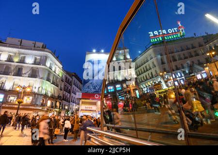 Menschenmassen in der Puerta del Sol, nachts mit dem berühmten Schild Tio Pepe, das sich in den Fenstern der Metrostation Sol widerspiegelt. Madrid, Spanien. Stockfoto