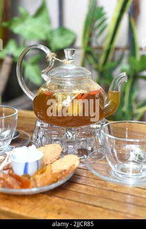 Kamillentee in einer Glas-Teekannen mit Tassen und kristallisierten Früchten Holztisch Stockfoto