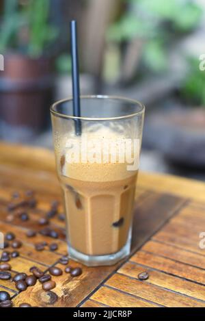 Espresso aus Iced Milk mit Kaffeebohnen auf Holztisch in Nahaufnahme Stockfoto