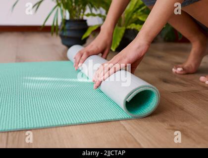 Eine junge, multiethnische Frau rollt ihre Yogamatte am Ende ihrer Praxis auf Stockfoto