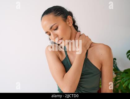 Eine junge, multiethnische Frau hält ihren Hals während des Yoga schmerzhaft fest Stockfoto