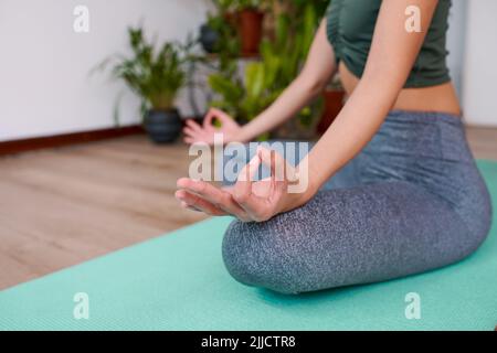Eine Nahaufnahme einer Frau, die auf einer Yogamatte sitzt, mit den Händen in Gyan Mudra, die Finger berühren sich Stockfoto