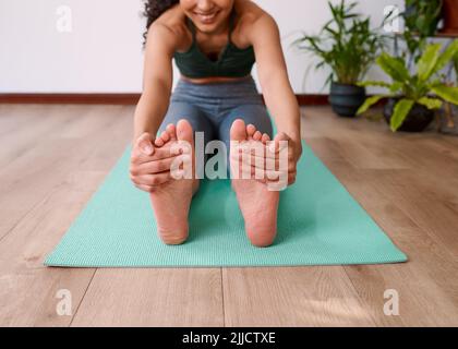 Nahaufnahme der Füße, während sich eine junge, multiethnische Frau auf einer Yogamatte ausdehnt Stockfoto
