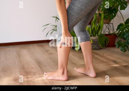 Eine Nahaufnahme einer jungen multiethnischen Frau, die ihr Kalb während des Yoga vor Schmerzen hält Stockfoto