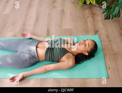 Eine junge, multiethnische Frau liegt am Ende der Praxis in der Shavasana-Yoga-Pose Stockfoto