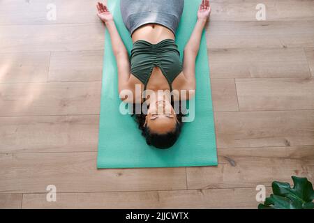 Eine junge, multiethnische Frau liegt am Ende der Praxis in der Shavasana-Yoga-Pose Stockfoto