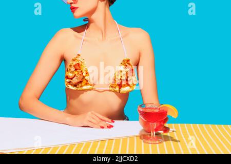 Zugeschnittenes Bild von weiblichem Körper, Cocktail auf gelber Tischdecke und Pizza-Element auf Stoff isoliert auf blauem Hintergrund Stockfoto