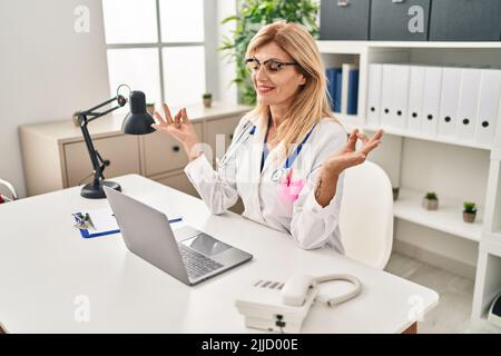 Blonde Frau mittleren Alters in der Ärzteinform, die in der Klinik Yoga-Übungen macht Stockfoto
