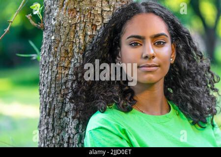 Outdoor-Porträt von schönen glücklich gemischt Rasse afroamerikanischen Mädchen Teenager weibliche junge Frau mit einem natürlichen grünen Blätter Hintergrund Stockfoto