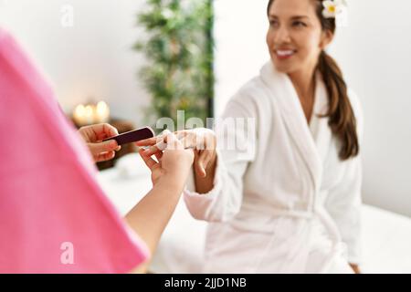 Junge latinerin im Bademantel bei Maniküre-Sitzung Stockfoto