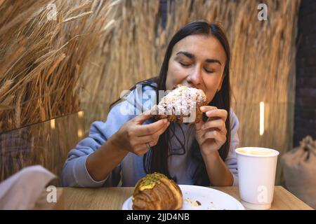 Eine junge Frau isst Croissants mit Kaffee in einem Café. Stockfoto