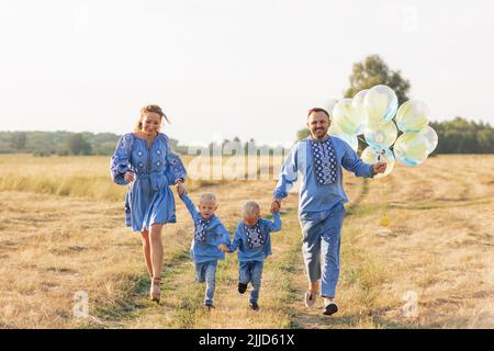 Glückliche Eltern mit zwei Zwillingssöhnen haben Spaß und laufen mit Luftballons auf der Wiese. Sie sind in ukrainische nationale bestickten Hemden gekleidet. Schließen Stockfoto