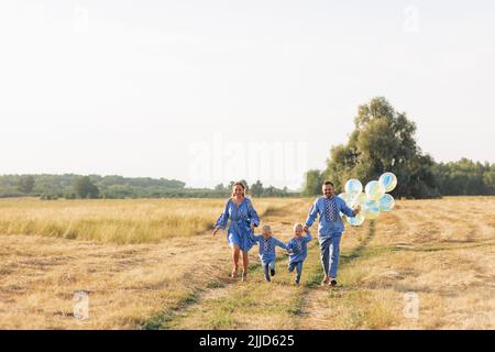 Glückliche Eltern mit zwei Zwillingssöhnen haben Spaß und laufen mit Luftballons auf der Wiese. Sie sind in ukrainische nationale bestickten Hemden gekleidet. Stockfoto